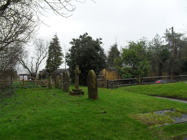 Un cementerio con cruces de piedra y lápidas, rodeado de árboles y un área cubierta de césped.