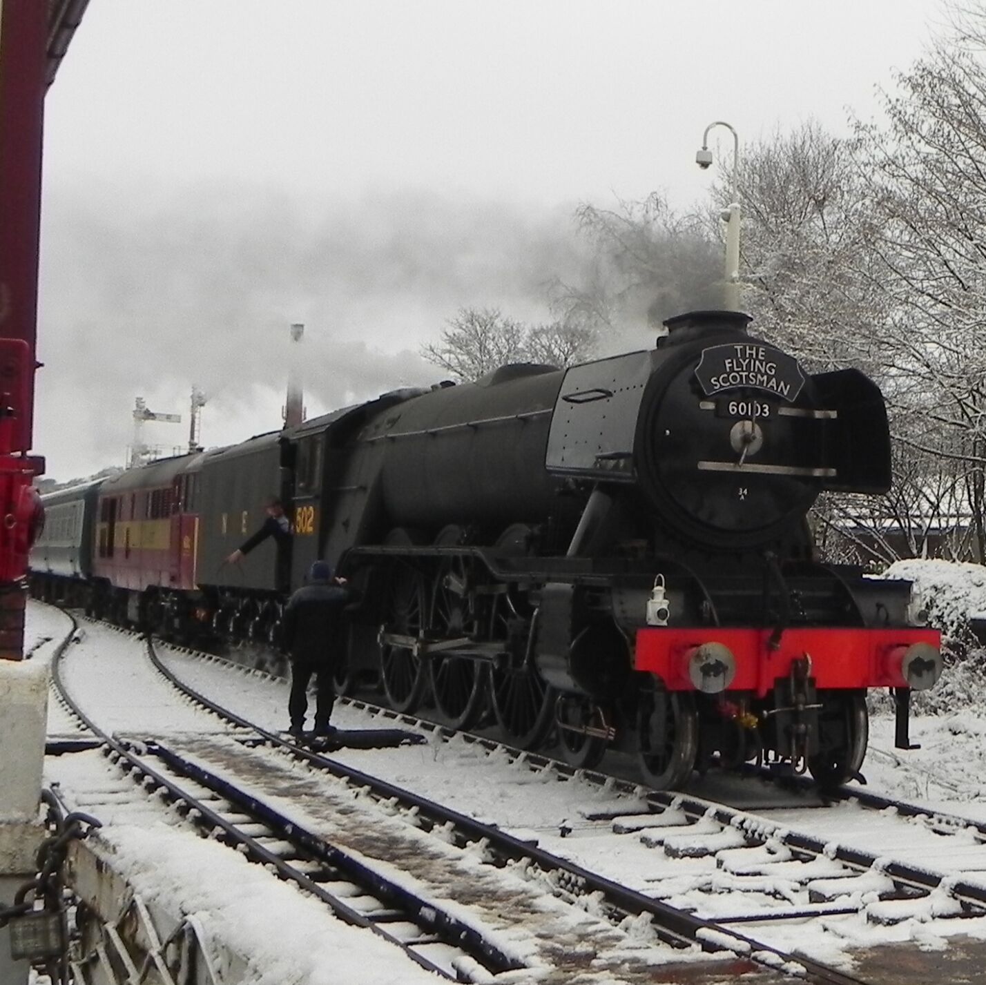A steam locomotive named 'The Flying Scotsman' with the number 60113, stationed on a snow-covered railway track.