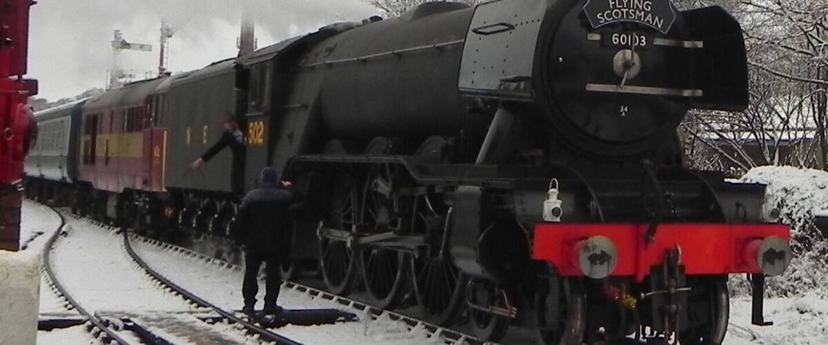 A steam locomotive named 'The Flying Scotsman' with the number 60113, stationed on a snow-covered railway track.