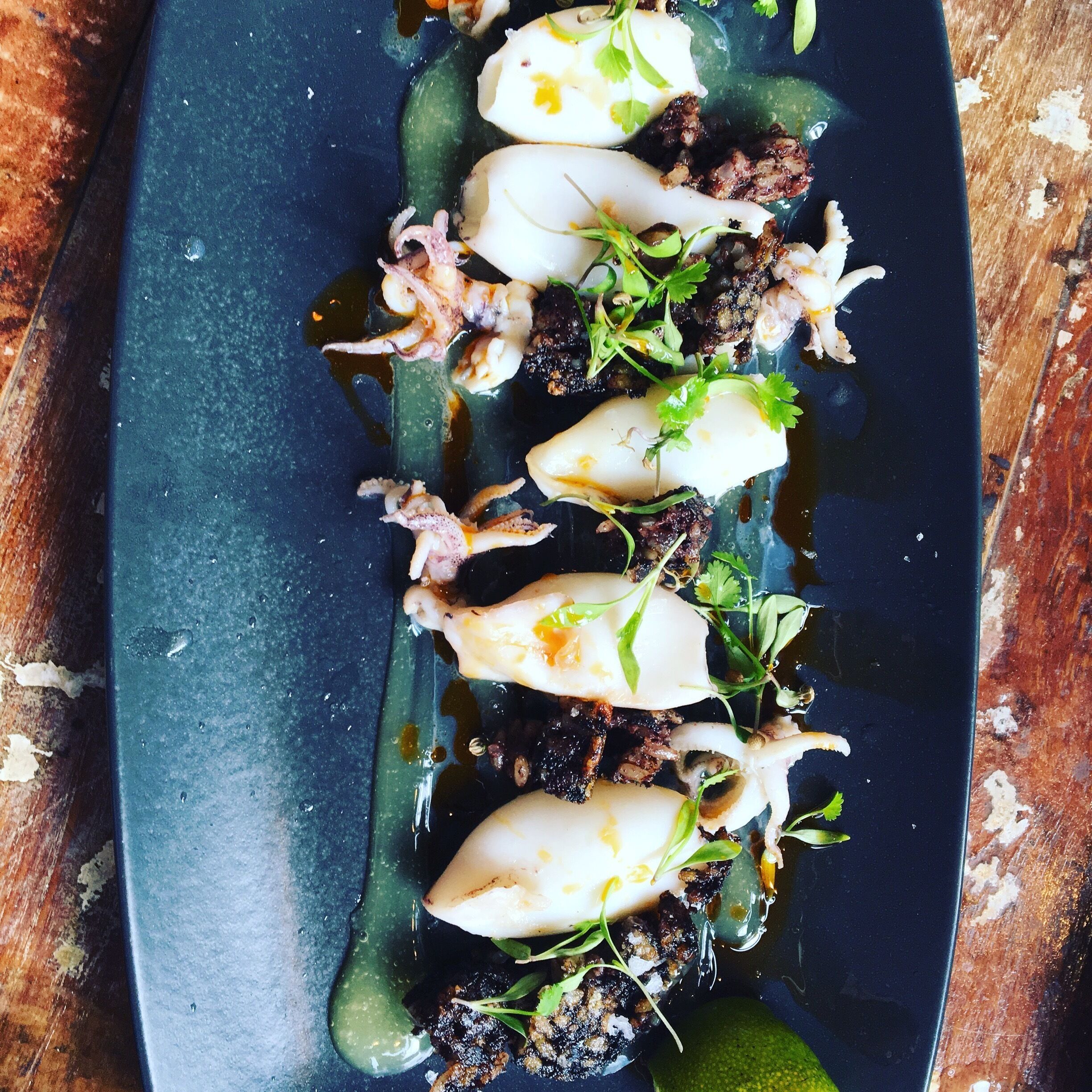 Un plato con tentáculos de pulpo, huevo y verduras sobre un fondo oscuro.