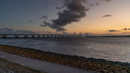A bridge over water with a rocky shoreline and a cloudy sky.