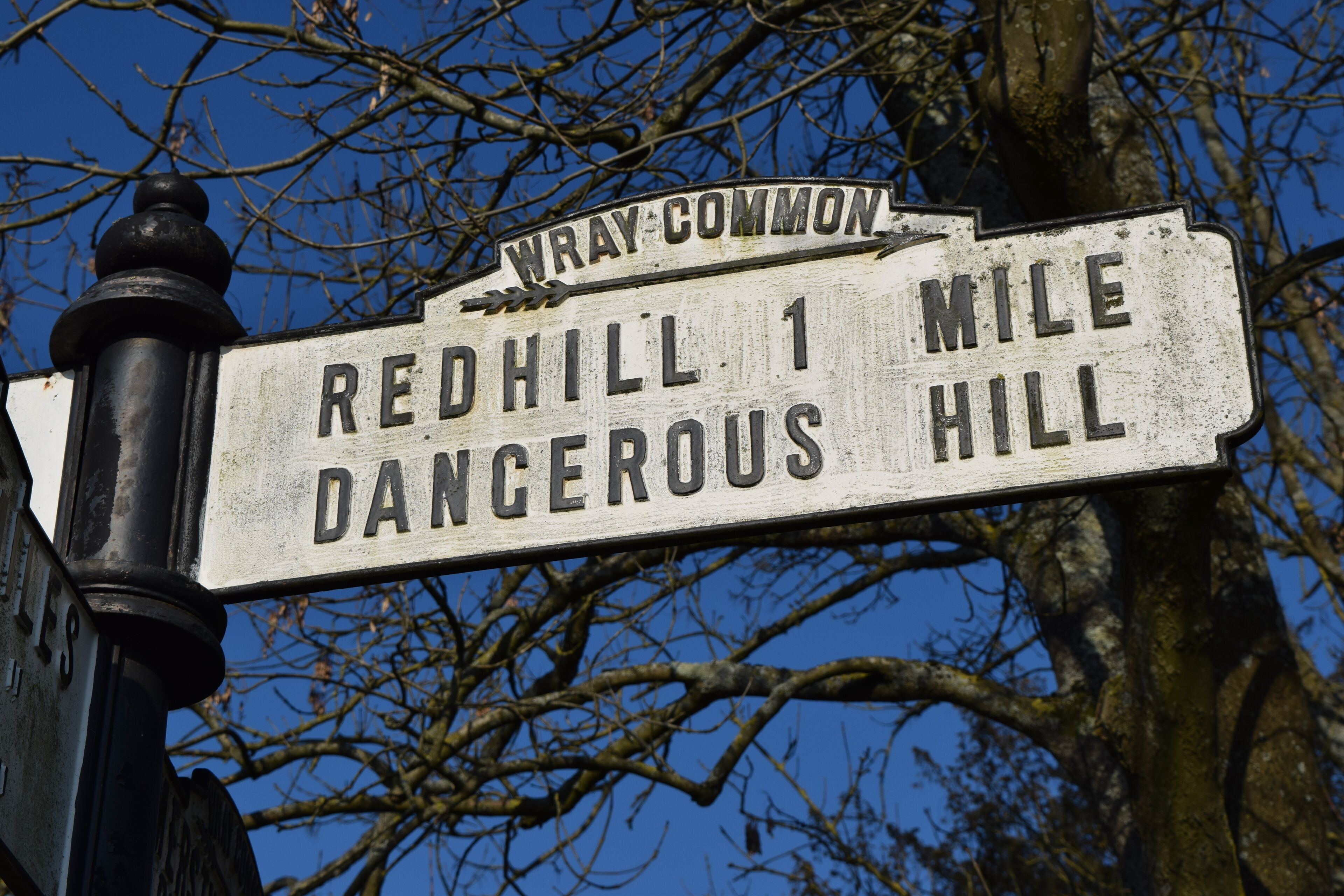 A weathered signpost with 'Wray Common' at the top and 'Redhill 1 Mile Dangerous Hill' below.