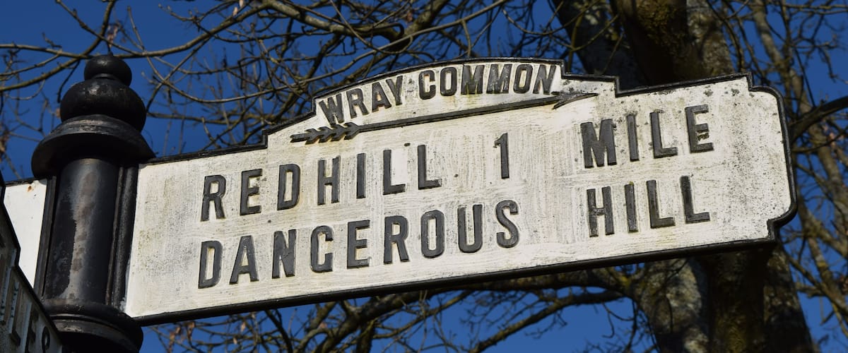 A weathered signpost with 'Wray Common' at the top and 'Redhill 1 Mile Dangerous Hill' below.