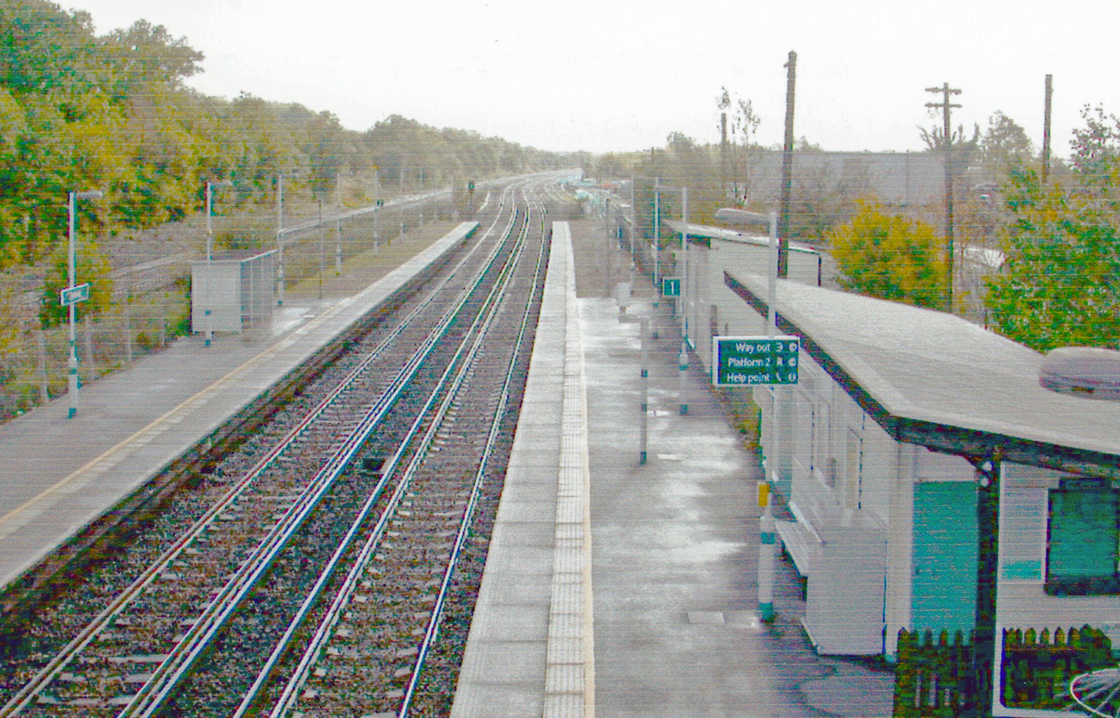 A train station with multiple tracks and a platform. There are signs indicating directions and a help point.