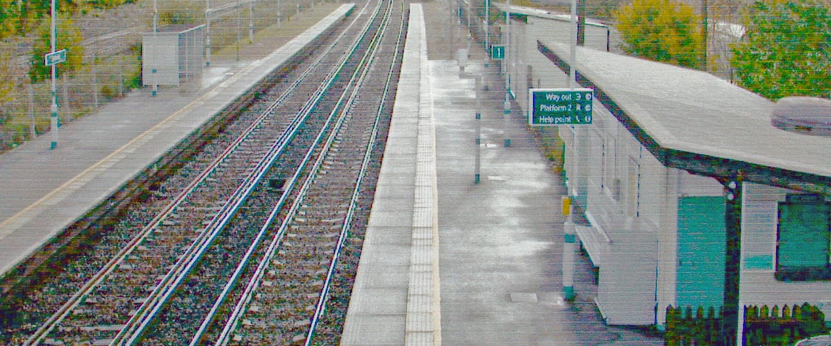 A train station with multiple tracks and a platform. There are signs indicating directions and a help point.