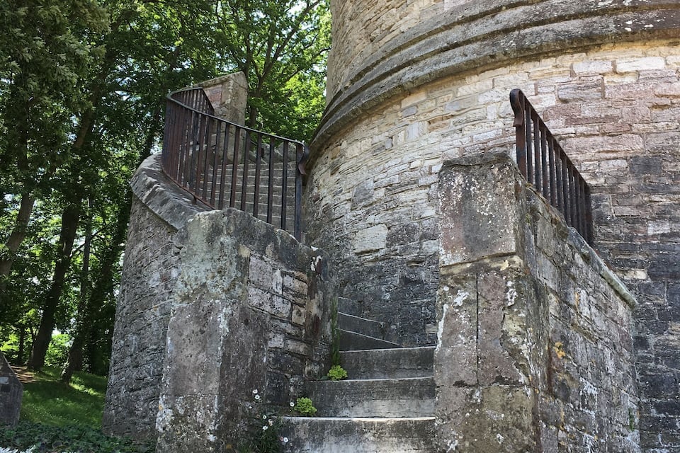 Eine Steintreppe führt zu einem Gebäude mit einem Türmchen und einem Metallgeländer.