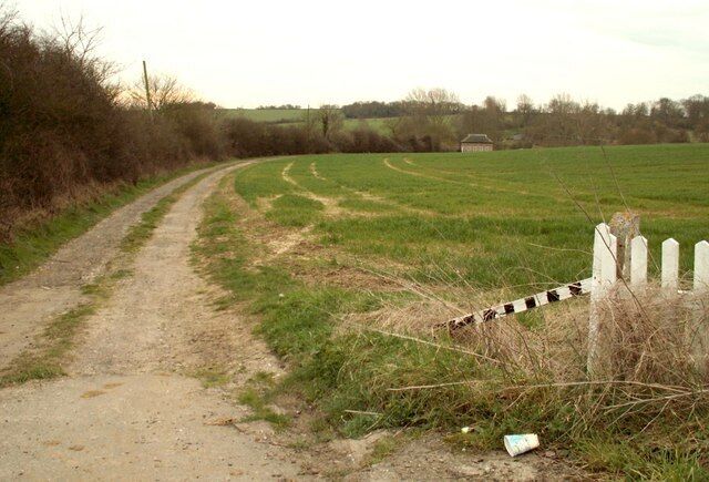 Un camino rural de tierra que serpentea por un campo con una cerca blanca y una reja.