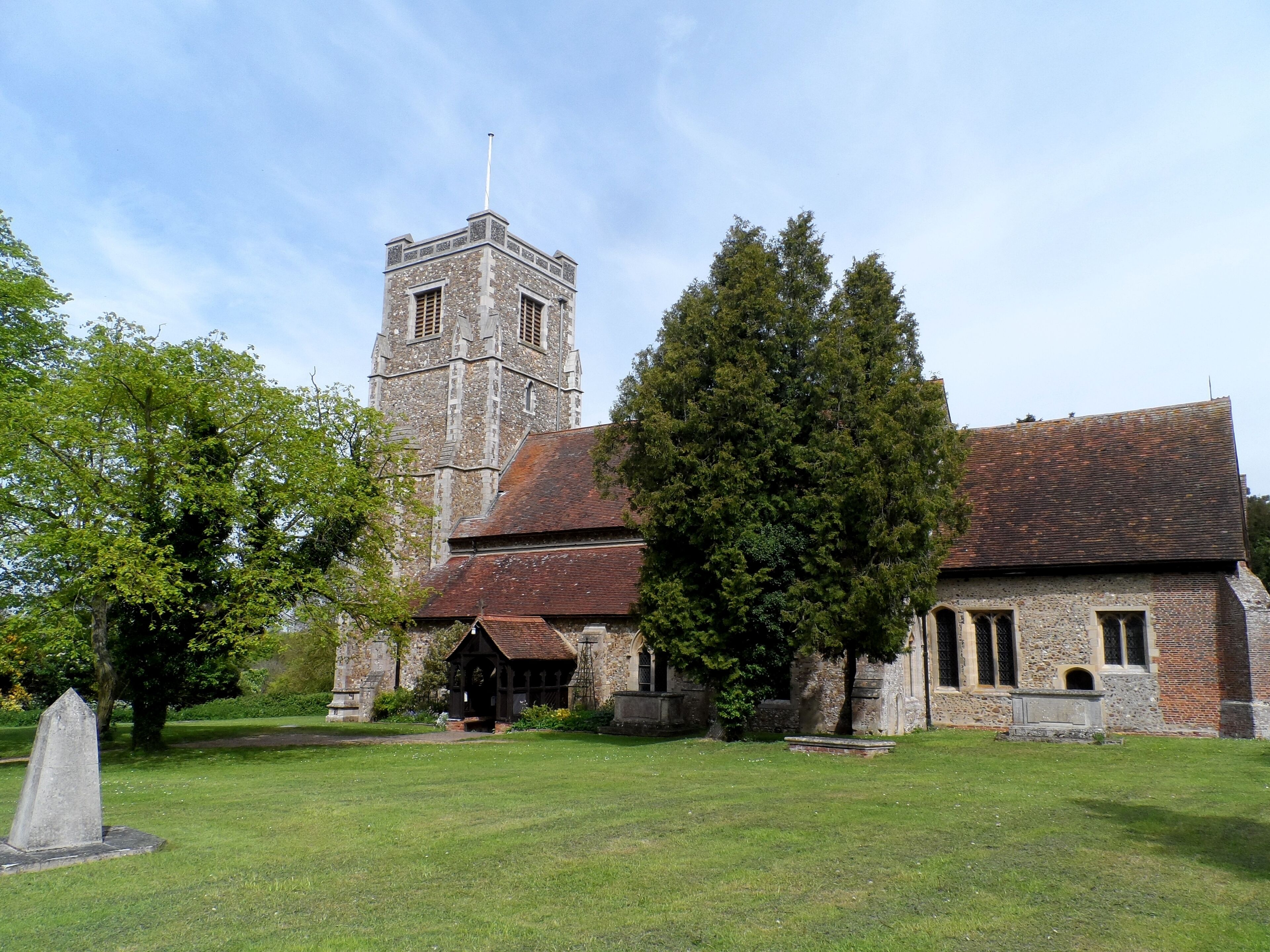 A historic church with a tall tower, surrounded by a well-maintained lawn and large trees.
