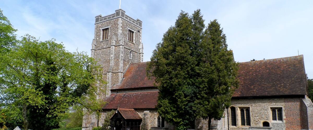 A historic church with a tall tower, surrounded by a well-maintained lawn and large trees.