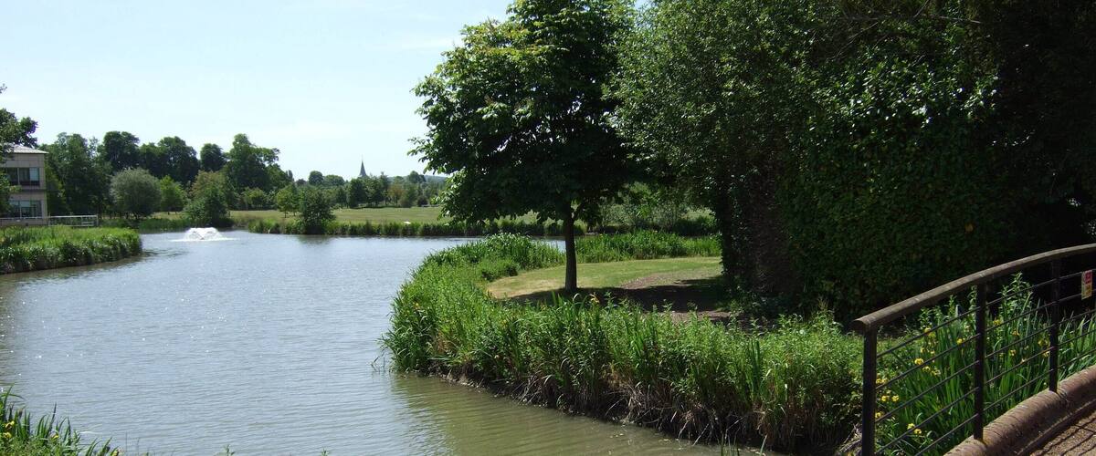 A calm river with a bridge, lush greenery, and a distant building.