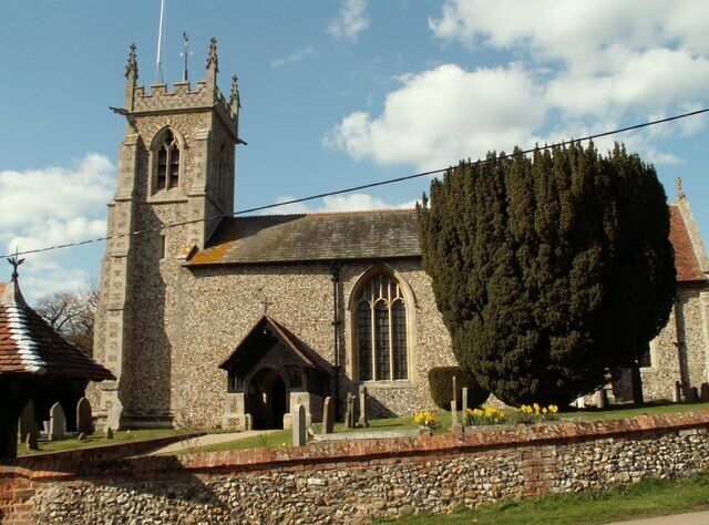 A historic stone church with a tall bell tower, a large tree in front, and a cemetery.