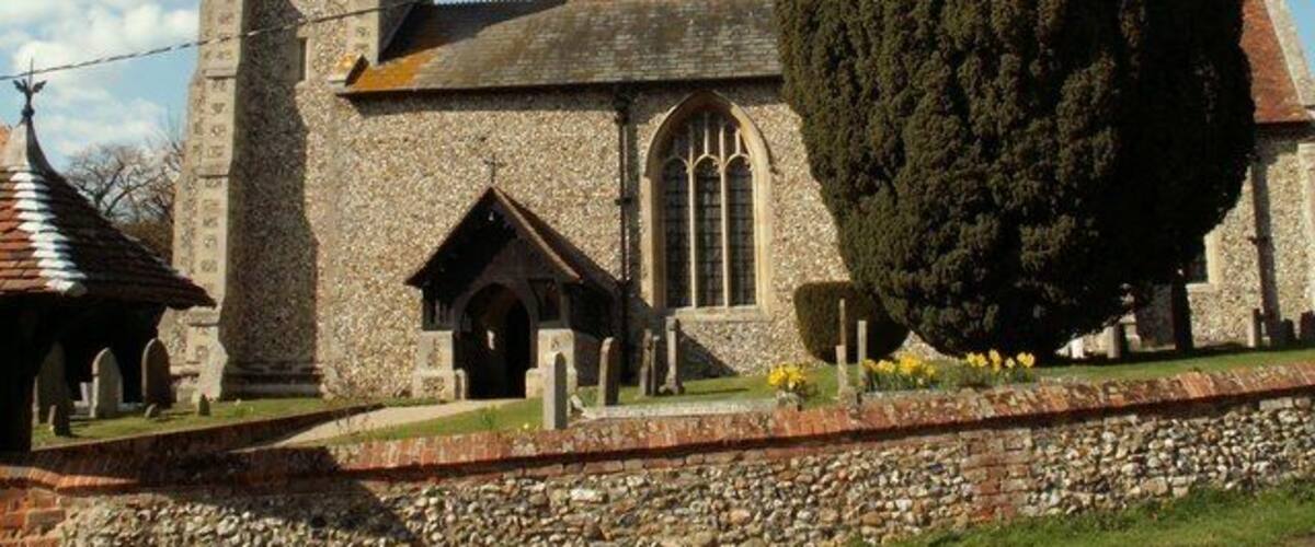 A historic stone church with a tall bell tower, a large tree in front, and a cemetery.