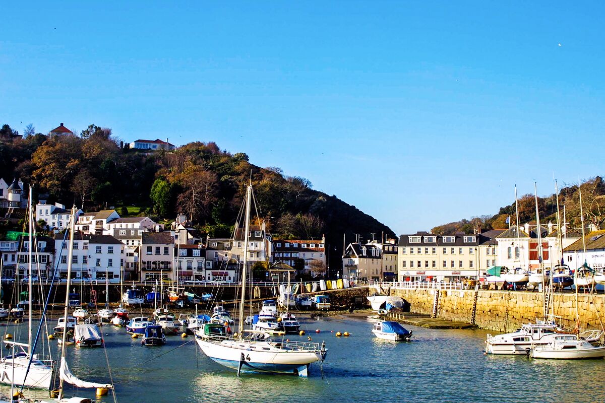 A harbor with numerous boats, a stone wall, and buildings on a hillside.