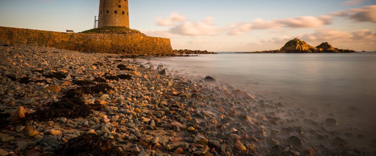 A rocky beach with a stone tower and a distant rocky island.