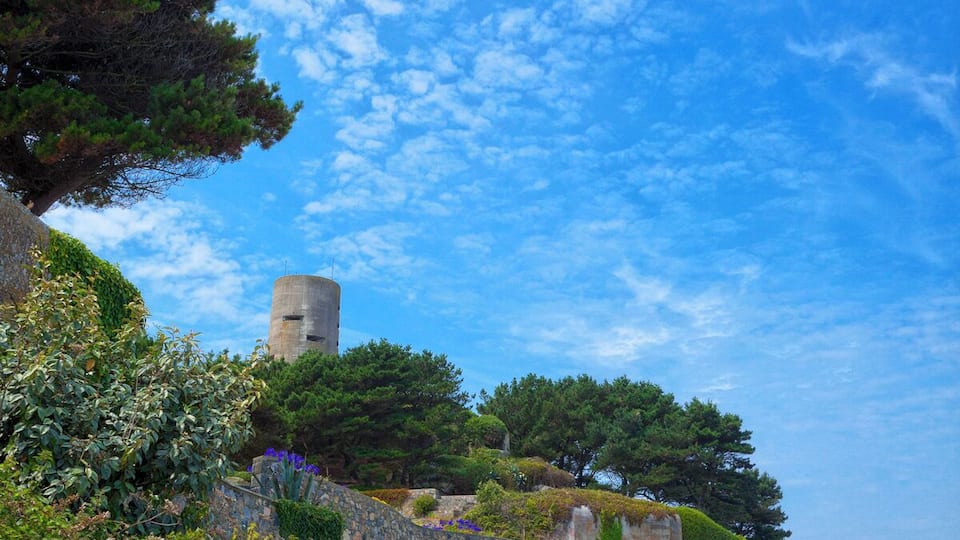 A stone pathway leading to a cylindrical tower surrounded by greenery and trees.
