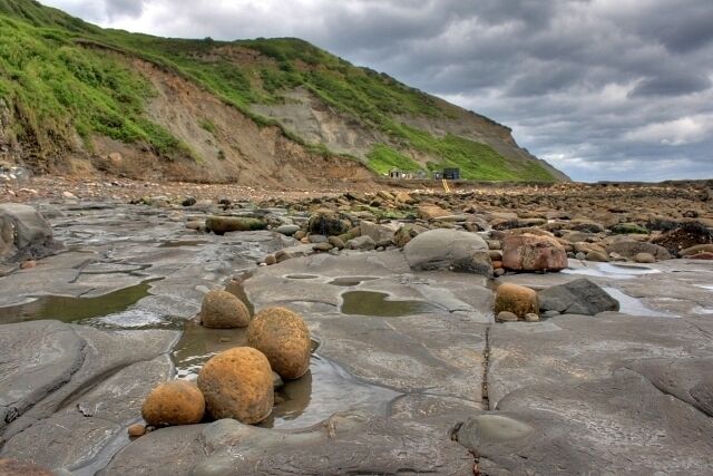 A rocky beach with large boulders and a green hillside in the background.