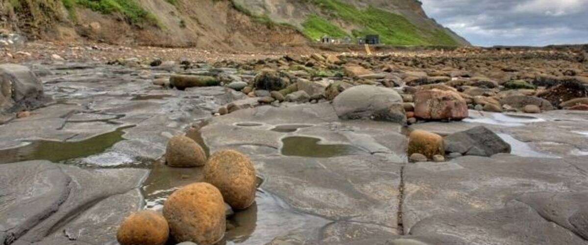 A rocky beach with large boulders and a green hillside in the background.