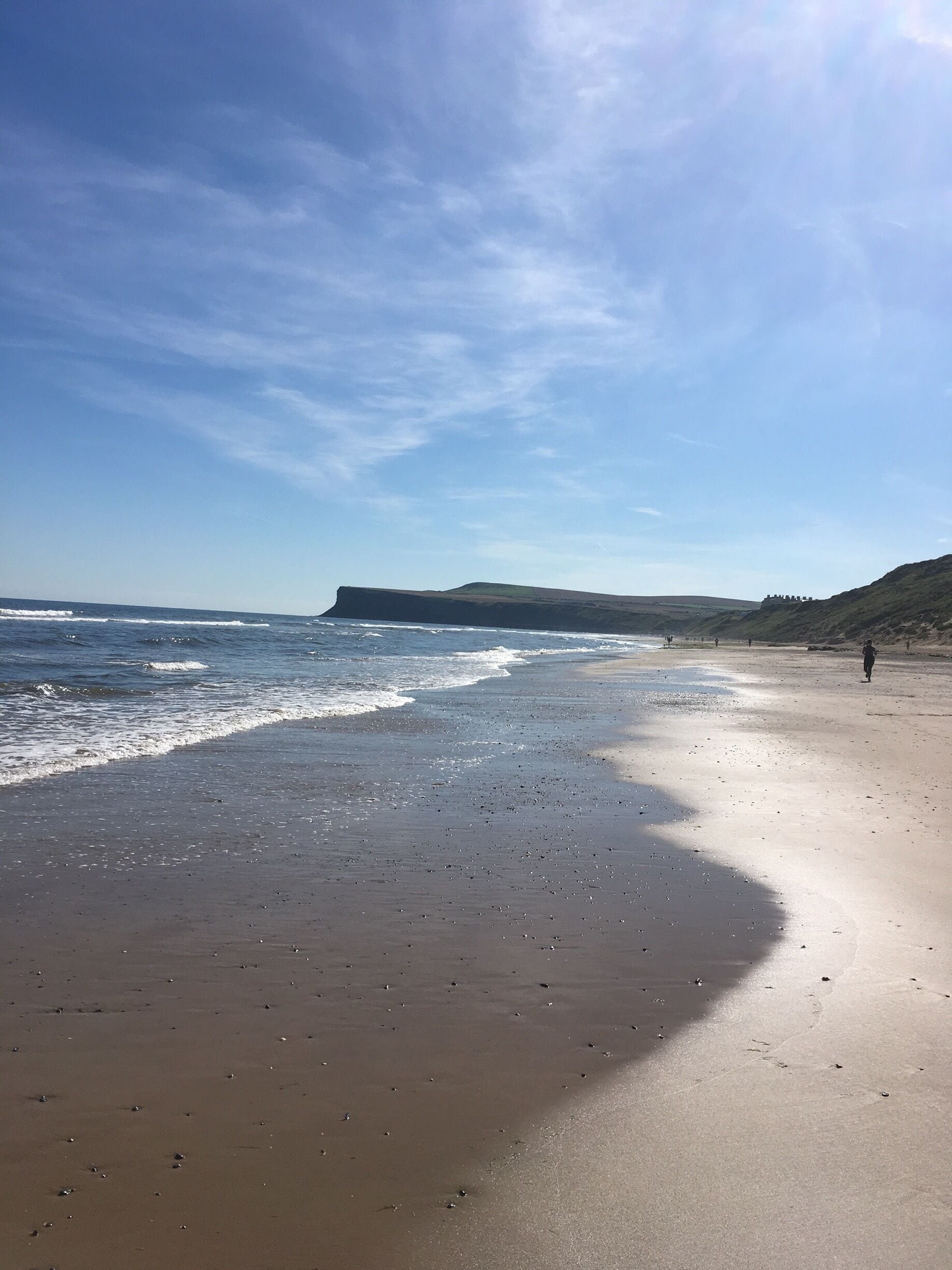 A sandy beach with gentle waves, a distant cliff, and a clear sky.