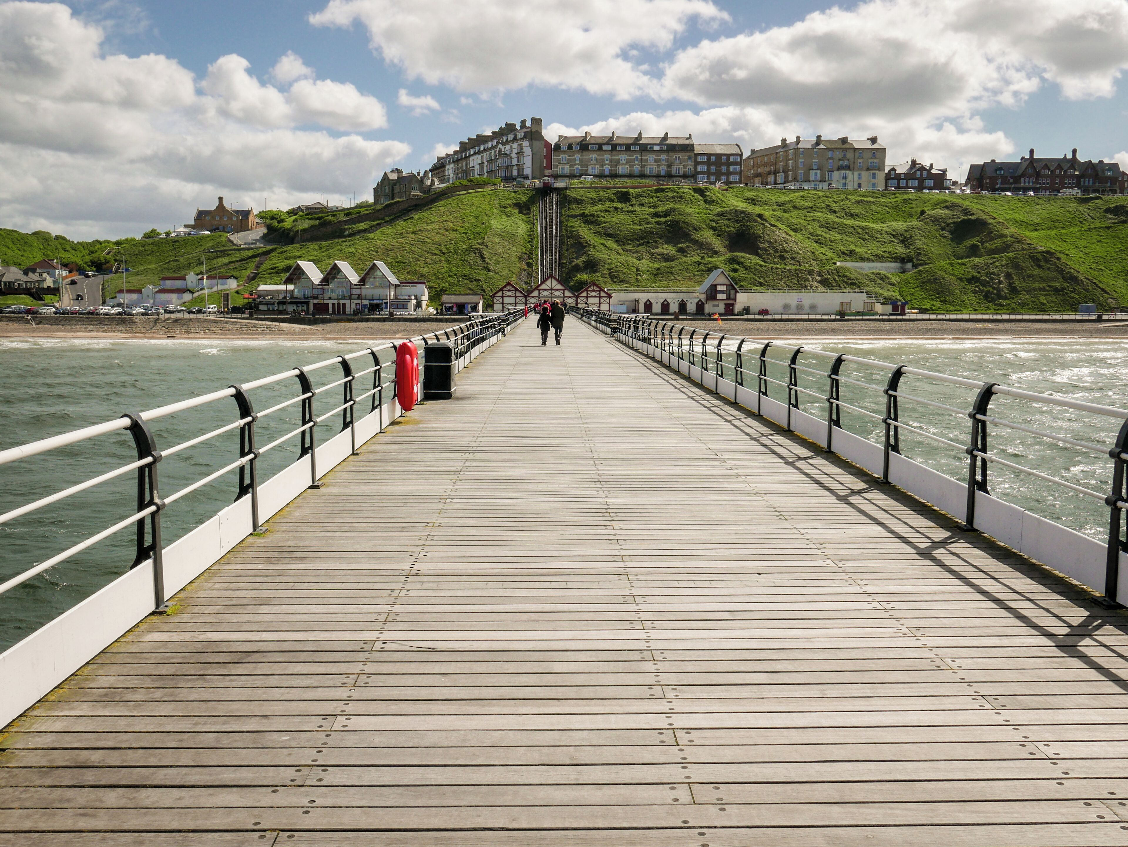 A wooden pier extending into the sea with a town in the background.
