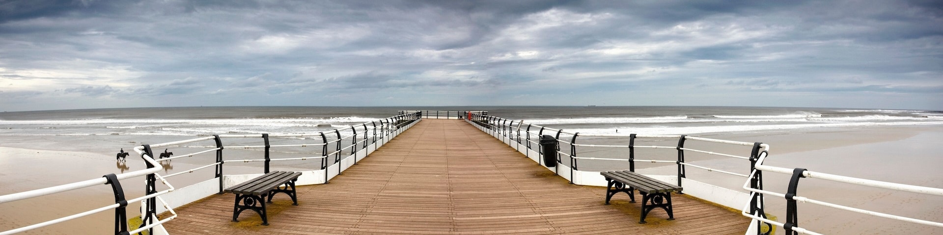 A wooden boardwalk leading to a beach with benches and railings.