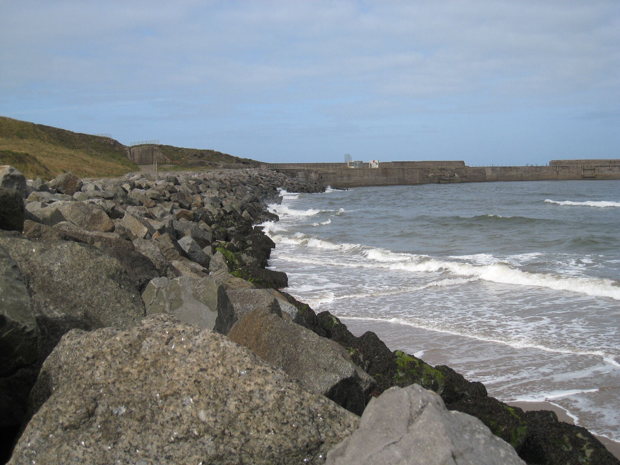 A rocky shoreline with waves crashing against a concrete sea wall.