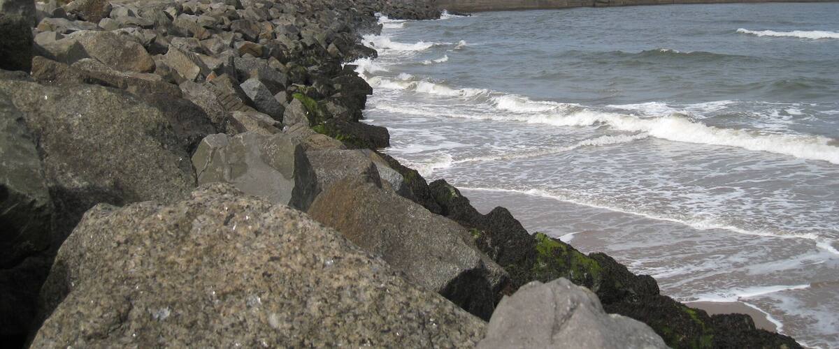 A rocky shoreline with waves crashing against a concrete sea wall.
