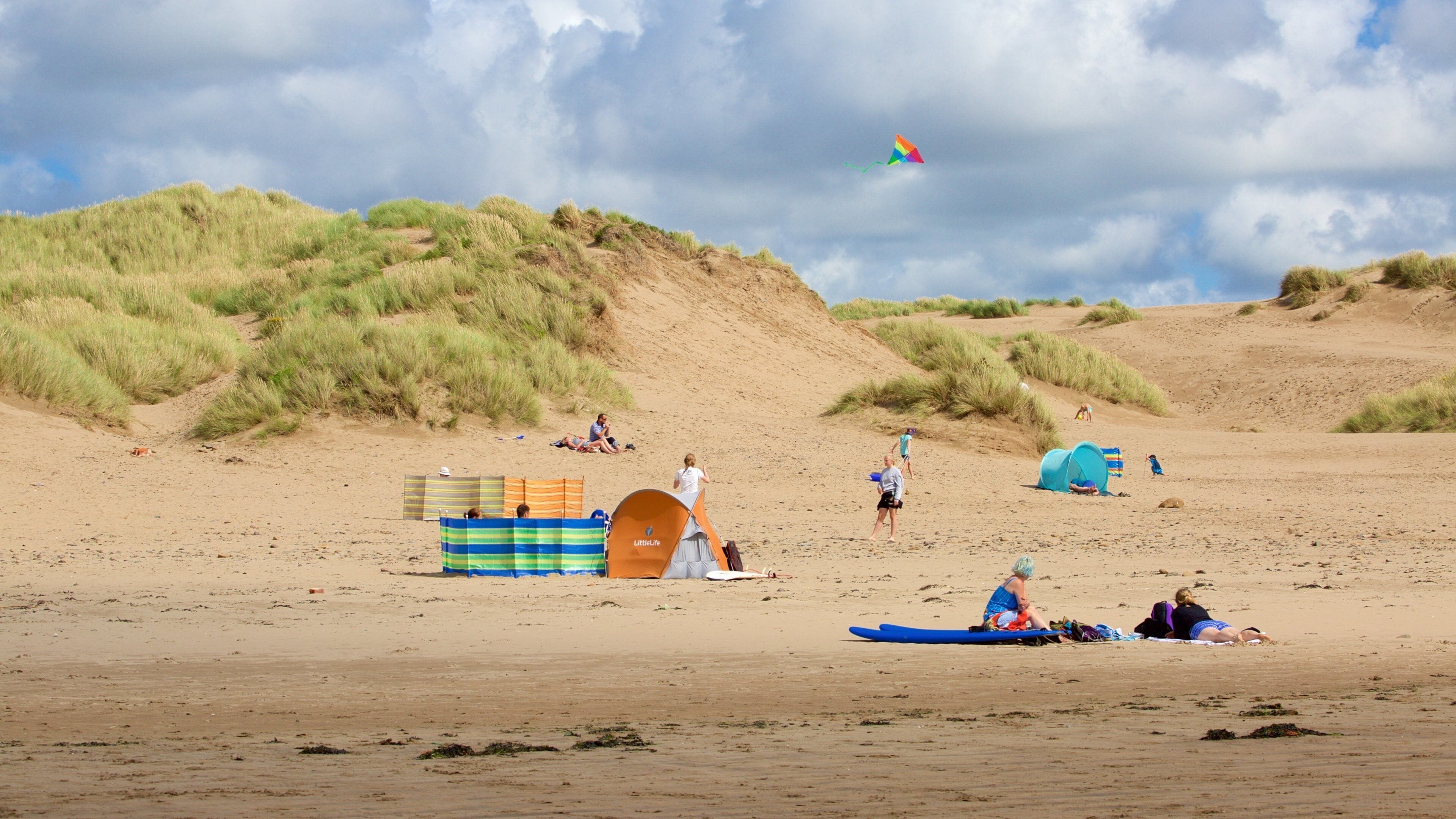 A sandy beach with dunes, tents, and people.