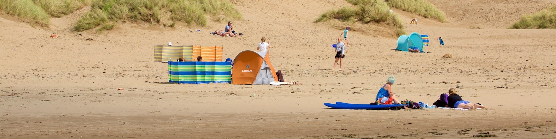 A sandy beach with dunes, tents, and people.