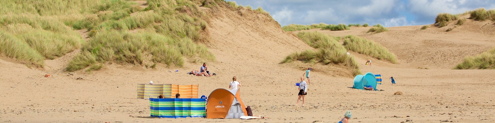 Ein Sandstrand mit Dünen, Zelten und Menschen.