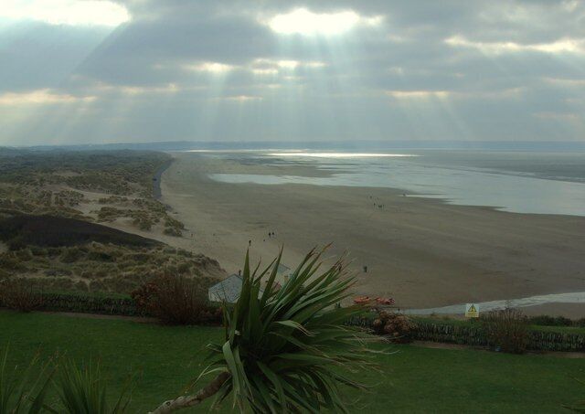 Paisagem costeira com praia de areia, dunas gramadas e um corpo de água.