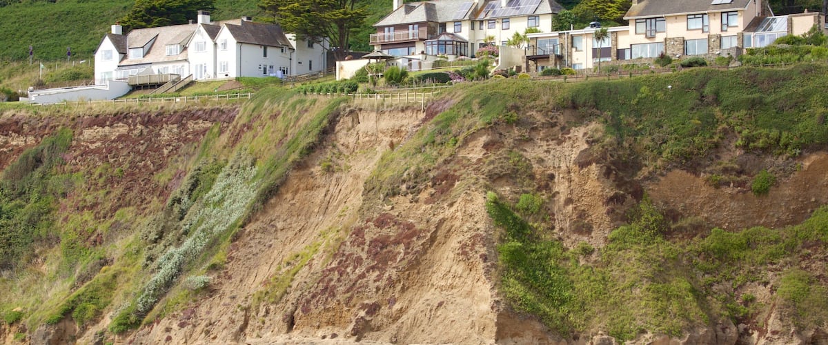 A coastal cliff with houses on top and people on the beach.