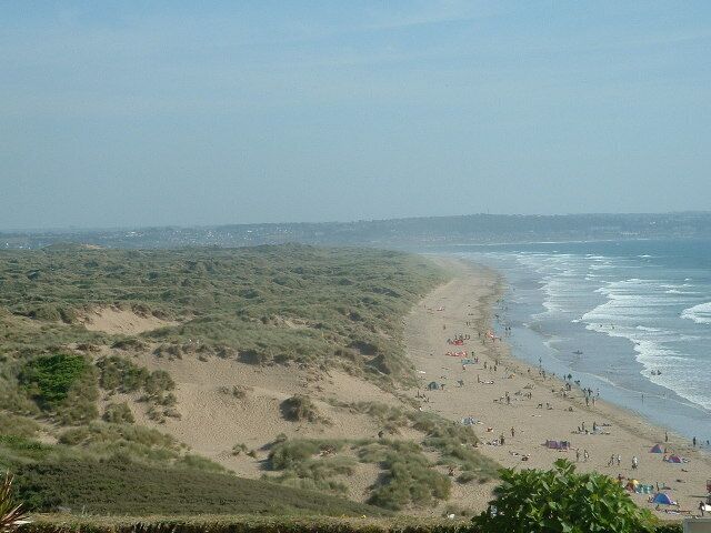 Paisagem costeira com praia arenosa, dunas e vista clara do oceano.