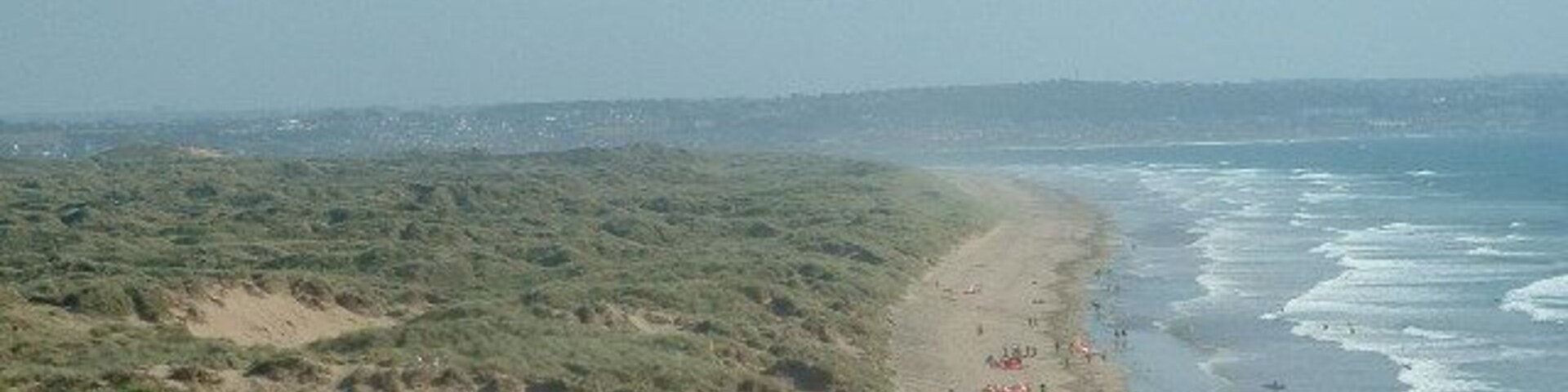 Paisagem costeira com praia arenosa, dunas e vista clara do oceano.