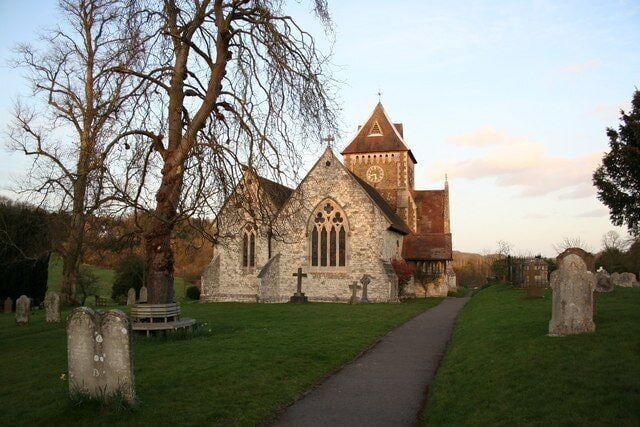 A stone church with a clock tower, surrounded by a cemetery with headstones.