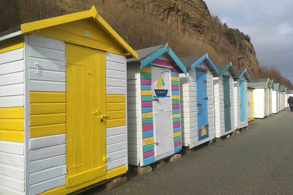 Een rij kleurrijke strandhutten langs een kustweg, met een klif op de achtergrond.