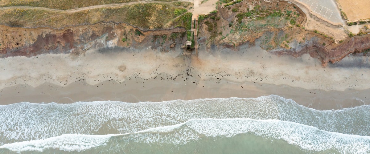 Aerial view of the waves crashing on the sandy shore of Compton Bay with rugged cliffs and coastal vegetation in Newport, Isle of Wight, United Kingdom.