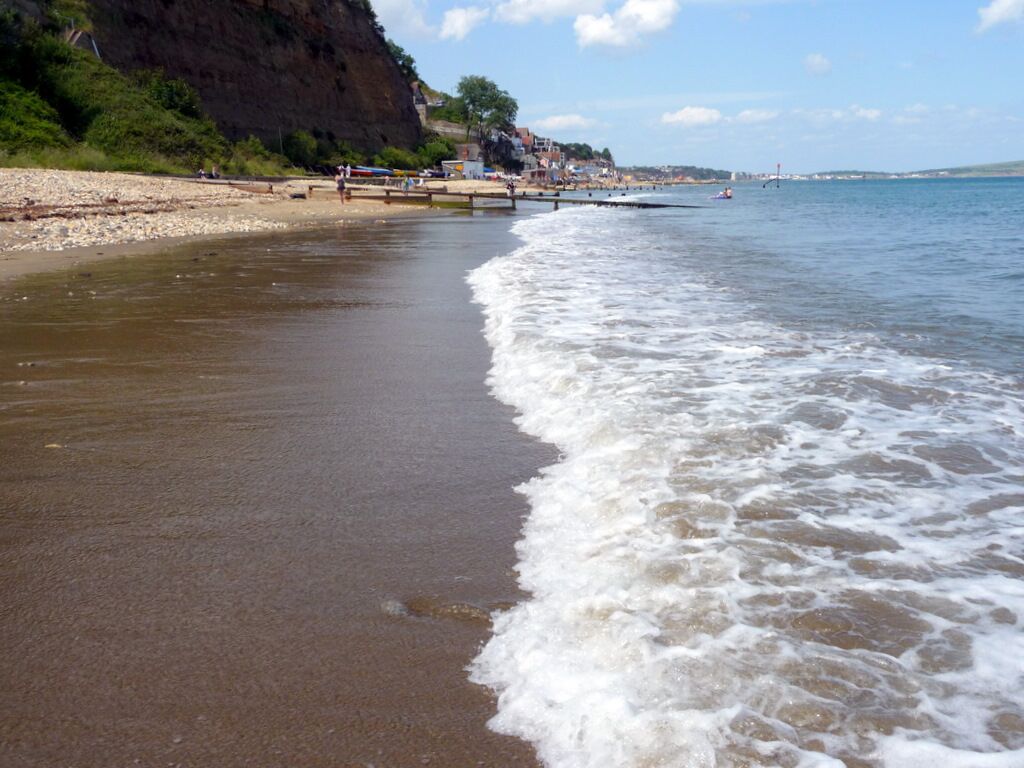 A beach with waves, a rocky cliff, and a pier.