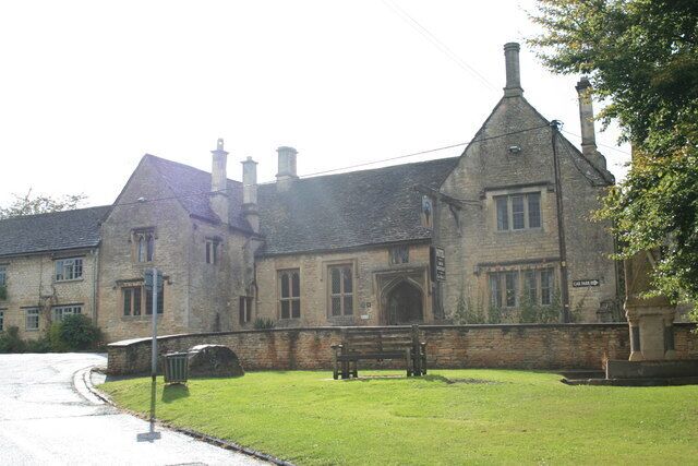 A large stone building with a steeply pitched roof, multiple chimneys, and a well-maintained lawn with a bench.