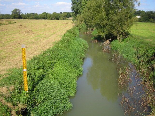 River Evenlode in Shipton under Wychwood Viewed looking upstream from the A361 road bridge, the Evenlode burst its banks in July 2007 causing severe flooding to low lying areas of Shipton under Wychwood. The yellow post with graduations is a water level gauge board. The top of the top black line above the top figure 9 is at 98 metres above sea level.
