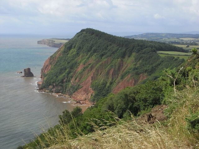A coastal landscape with a prominent green hill, a rocky outcrop, and a view of the sea.