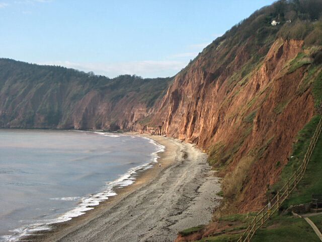 A coastal landscape with a sandy beach, steep cliffs, and a clear sky.