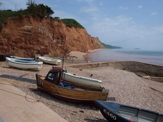 A rocky beach with several small boats, cliffs, and calm water.