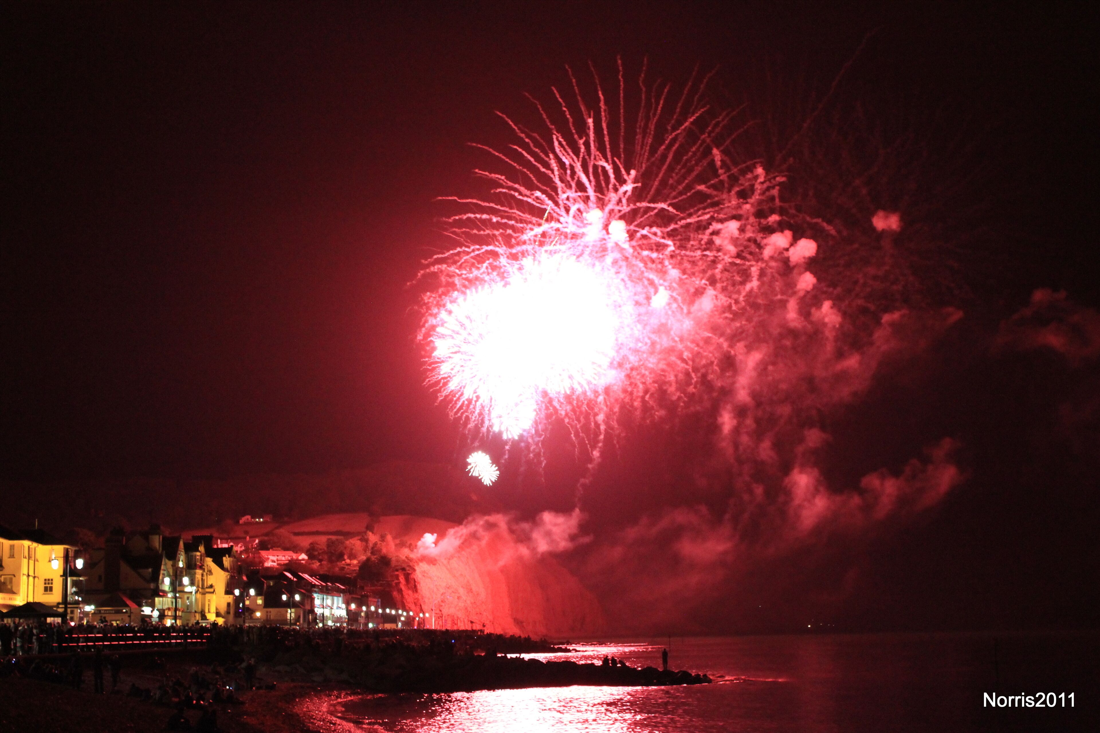 A night scene with fireworks over a coastal town.