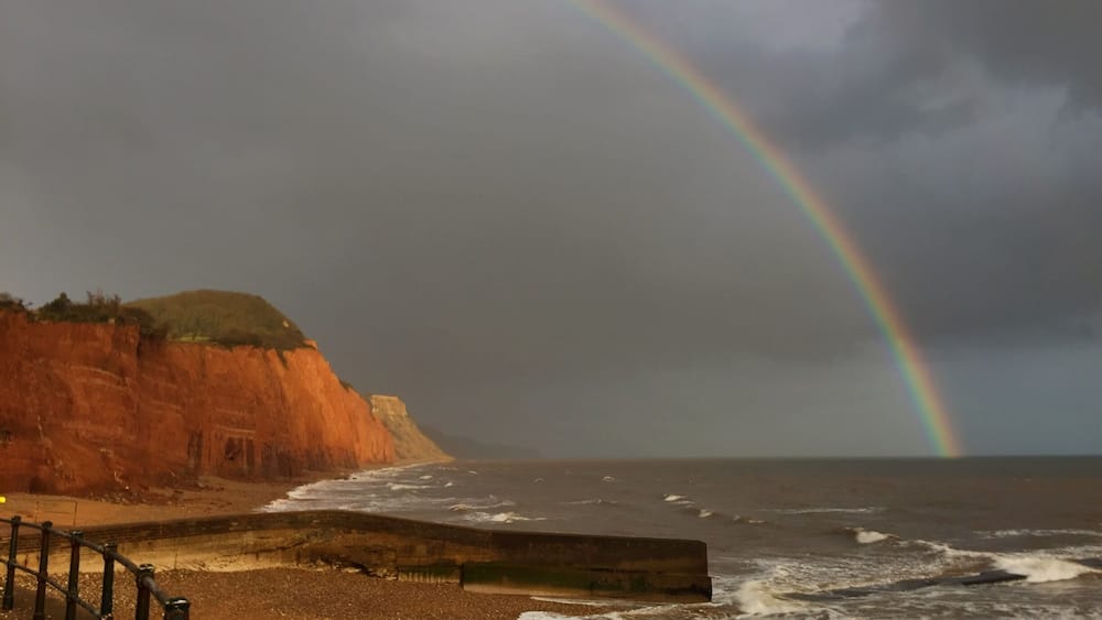 Ein Strand mit einer Klippe, Meereswellen und einem Regenbogen.