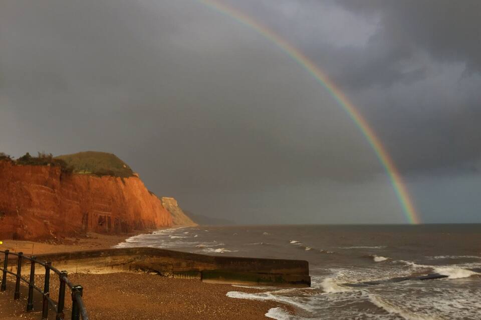 A beach with a cliff, ocean waves, and a rainbow.