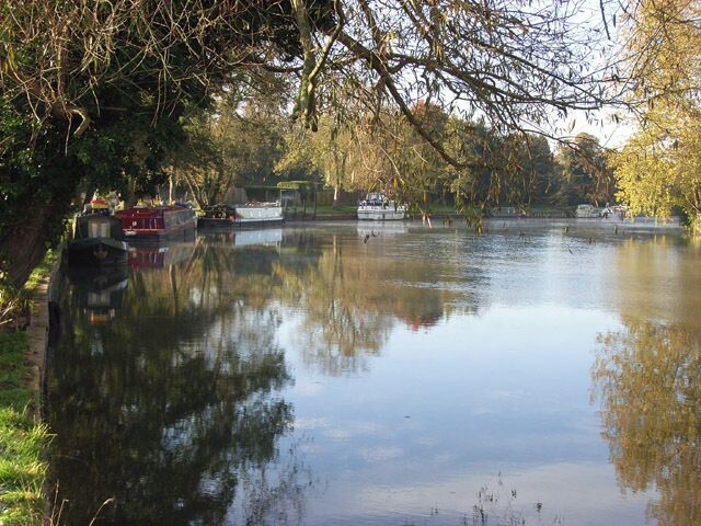 A calm river with boats, trees, and a bridge.