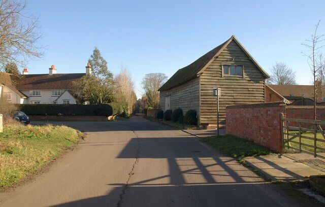 A rural road with a wooden barn, houses, and a car parked on the side.