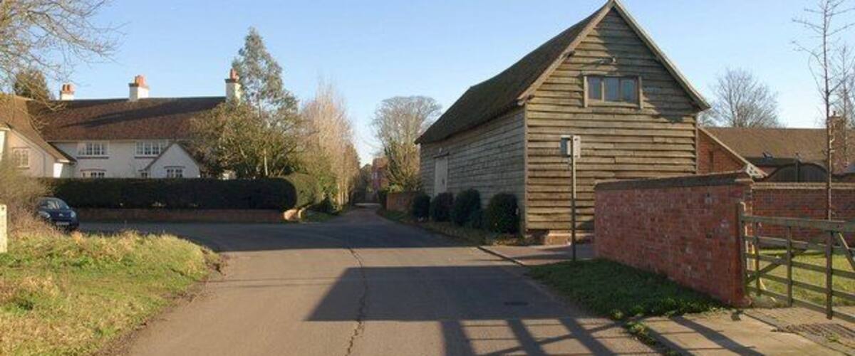 A rural road with a wooden barn, houses, and a car parked on the side.