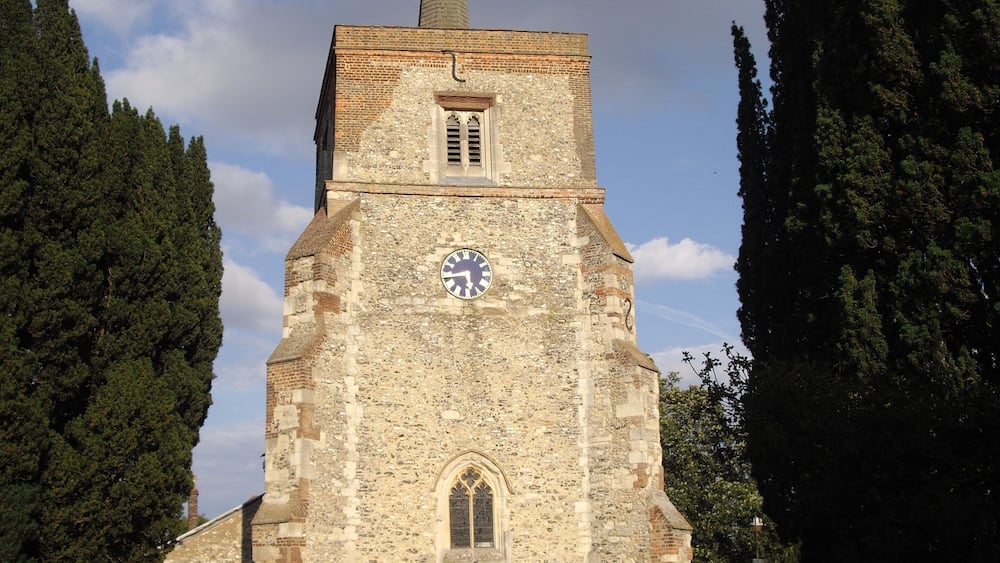 Une église dotée d’un clocher, entourée d’arbres et d’un cimetière.