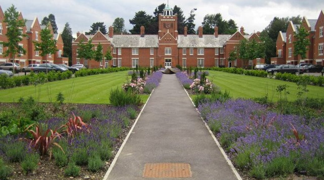 London Colney: Napsbury Park The building at the end of the path with its clock tower was the Main Ward of the former Napsbury Hospital. The hospital was built, in its country house and grounds style setting, between 1898 and 1905 to the design of Rowland Plumbe. It was designed to accommodate some 1,200 long stay patients who through illness were unable to make a full contribution to society. The hospital closed in 1998 and the site and buildings have since been refurbished to create The Arboretum estate. A look at the Google satellite imagery, which currently shows the state of the hospital before the changes were made, reveals how many buildings were demolished to open up this vista. The houses on either side of the square are new.